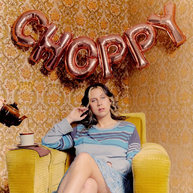 Album cover for Grace Robinson's Choppy: singer sits in a yellow armchair under foil balloons spelling 'choppy' as tea is poured into a mug.